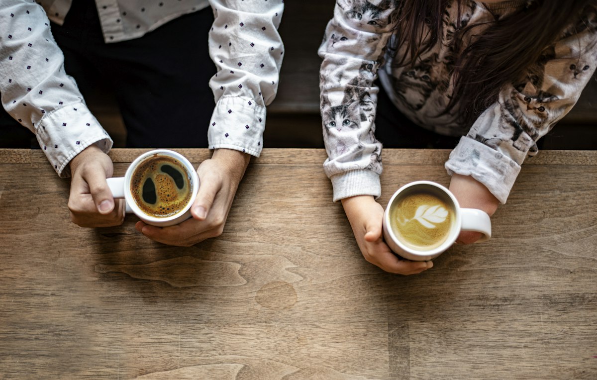 Two people sitting with cups of house-roasted ConnectionCafe.com coffee at a wooden table in Shoreditch