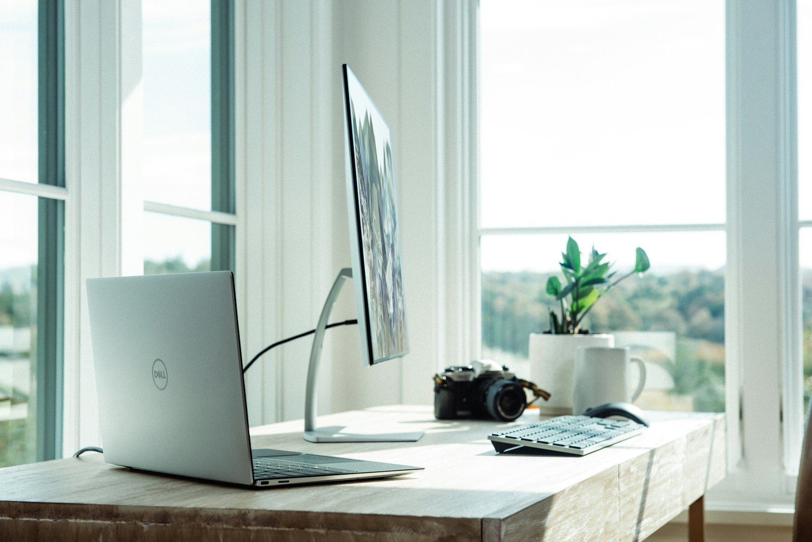 A laptop and monitor on a white home-office desk by a window