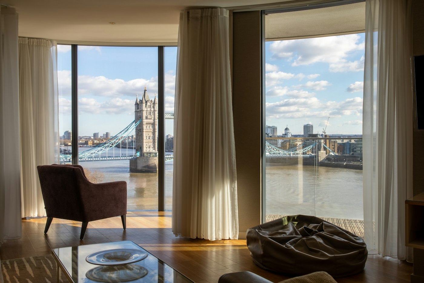 Top-floor hotel suite with a large window, armchair and morning light over the city