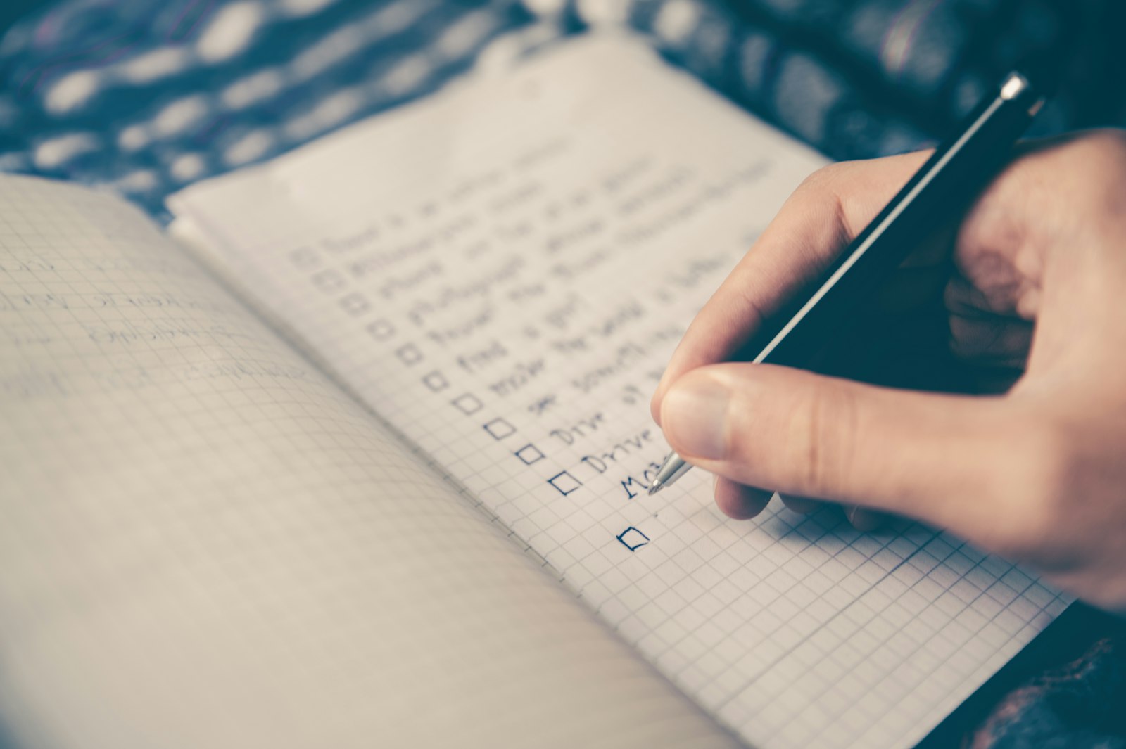 A hand writing a checklist in a squared notebook