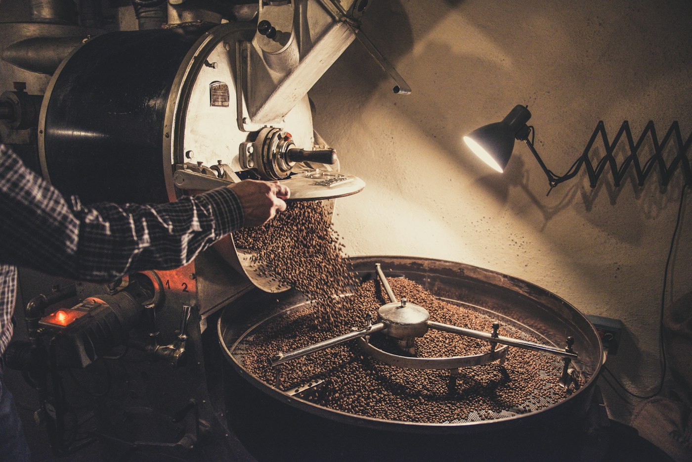 A roaster tipping green coffee beans into a drum roaster in the ConnectionCafe.com basement roastery